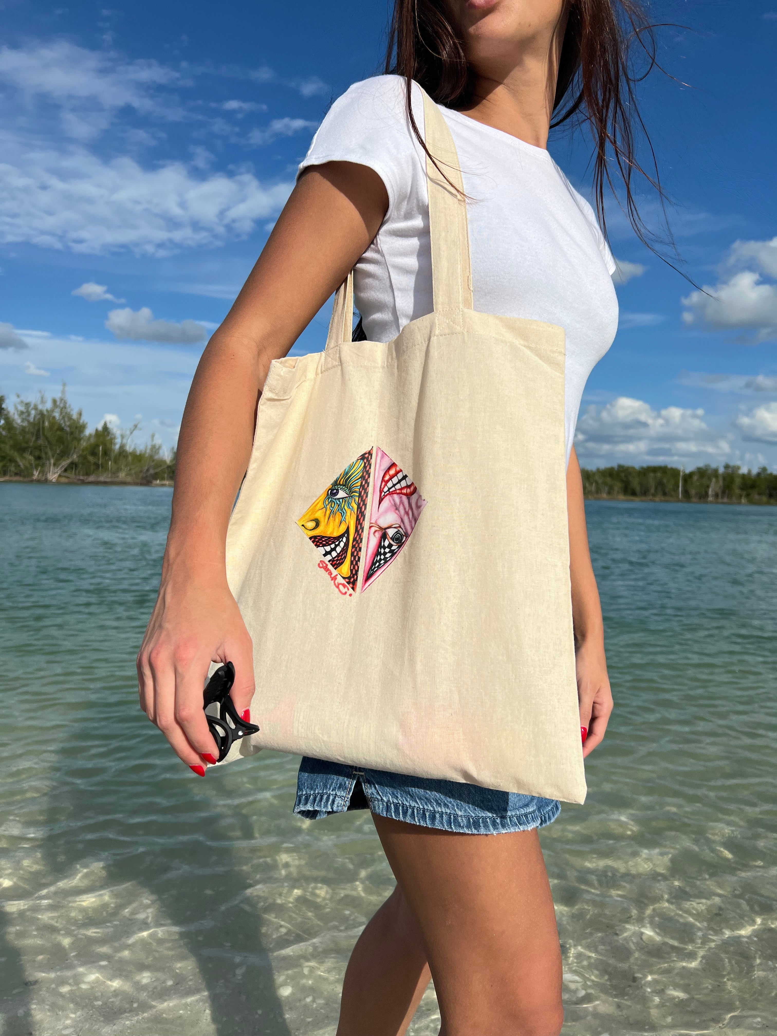 Person holding a tote bag with a psychedelic design by a body of water